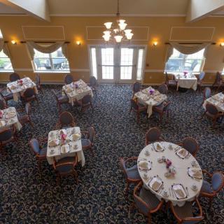 An elegantly set dining room with multiple tables and chairs, featuring warm lighting and a carpeted floor.