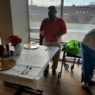 A man stands by a dining table in a restaurant with flowers and a wheelchair nearby.