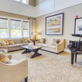 A spacious and elegantly decorated living room featuring comfortable sofas, a grand piano, and large windows.