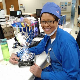 A dedicated nurse proudly holds a trophy in a hospital setting, celebrating her achievements.
