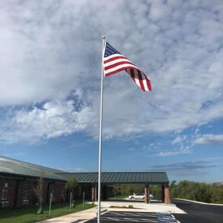 An American flag waving on a flagpole in front of a building under a cloudy sky.