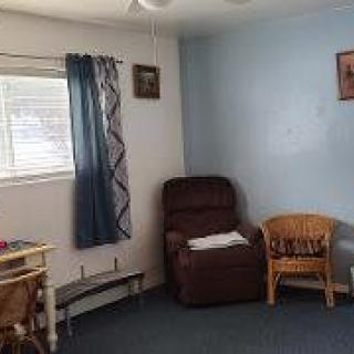 A cozy living room featuring a brown recliner, wicker chair, and blue curtains by the window.