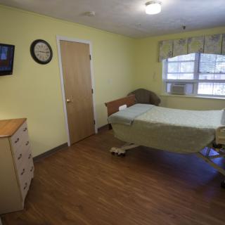 A simple hospital room with a single bed, TV, and window.