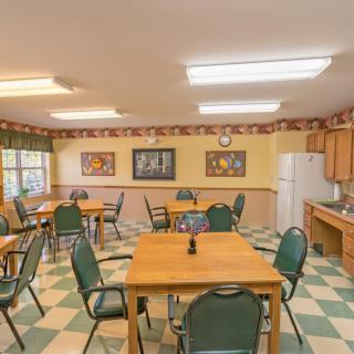 A communal dining room with several tables and chairs, featuring a checkered floor and wall-mounted artwork.