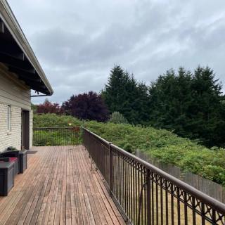 A spacious wooden deck with a view of lush greenery and a cloudy sky.