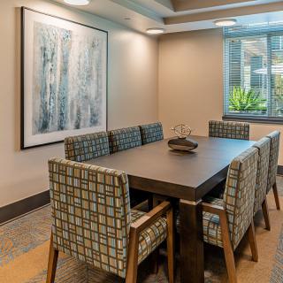 A modern dining room featuring a rectangular table and patterned chairs, adorned with contemporary artwork on the wall and natural light streaming through the window.