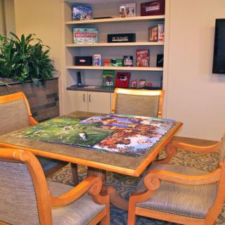 A cozy room with a table featuring a jigsaw puzzle, surrounded by chairs and shelves displaying board games.