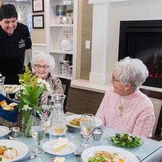 A group of seniors enjoying a meal together at a dining table with a server attending to them.