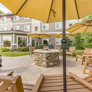 A cozy outdoor patio with yellow umbrellas, wooden chairs, and a central stone fire pit.