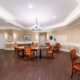 A spacious dining area with wooden flooring, featuring tables and chairs arranged neatly under elegant lighting.