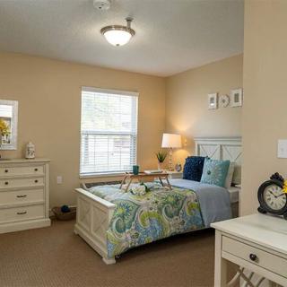 A cozy bedroom interior with a bed, dresser, and bedside lamp.
