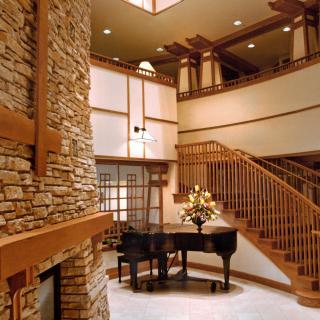 A modern interior featuring a grand piano, stone fireplace, and elegant wooden staircase.
