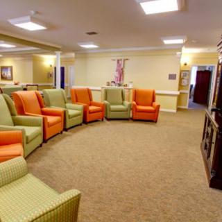 A spacious room with a circular arrangement of green and orange chairs, featuring a carpeted floor and soft lighting.