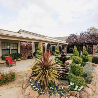 A beautifully landscaped garden with a central fountain in front of a house.