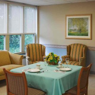 A cozy dining area with a teal tablecloth, surrounded by comfortable chairs and a sofa, adorned with a framed painting on the wall.