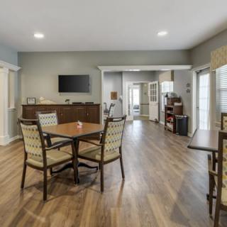 A modern living room and dining area with wood flooring, featuring a table, chairs, and a wall-mounted TV.