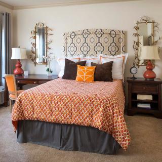 A well-decorated bedroom featuring a bed with orange patterned bedding, flanked by two bedside tables with matching lamps and ornate mirrors.
