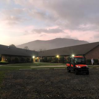 A serene evening view of a building with mountains in the background and a tractor parked nearby.
