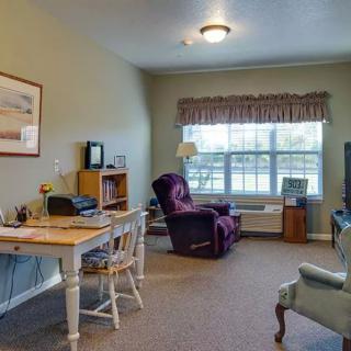 A cozy living room with a desk, chairs, and a large window allowing natural light.