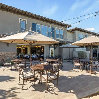 An outdoor patio with tables, chairs, and umbrellas at a cafe or restaurant on a sunny day.