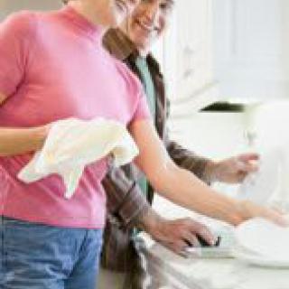 A couple washing dishes together in the kitchen.