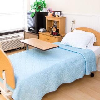 A tidy hospital room with a neatly made bed and a small over-bed table.