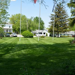 A suburban yard with a neatly mowed lawn, surrounded by trees and homes, featuring several flagpoles under a clear sky.