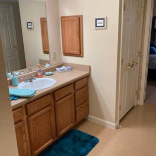 A bathroom with a sink, mirror, and wooden cabinets, featuring teal towels and a bath mat.