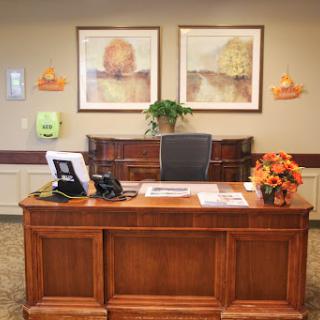 A warm and inviting office reception area featuring a wooden desk, decorative artwork, and floral arrangements.