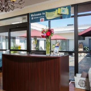 A hotel reception area with a wooden desk and flower arrangement, overlooking a courtyard.