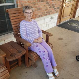 An elderly woman enjoys a peaceful moment outdoors, sitting comfortably in a wooden chair.