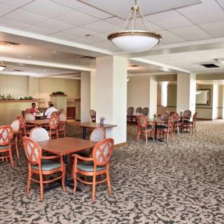 A spacious dining area with multiple tables and chairs, featuring patterned carpet and overhead lighting.