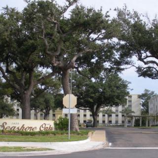 Entrance to a residential area with large trees and buildings in the background.