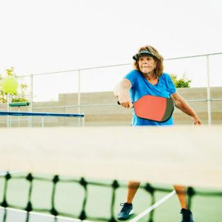 A person playing pickleball on an outdoor court, focusing on hitting the ball with a paddle.