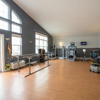 A well-lit rehabilitation therapy room with exercise equipment and large windows.