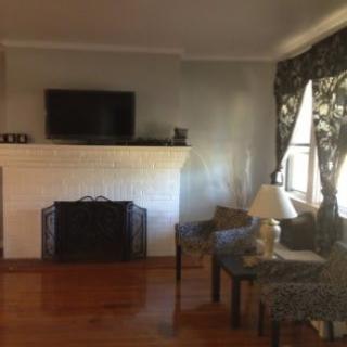 A cozy living room with a fireplace and television, featuring chairs and a lamp by the window.