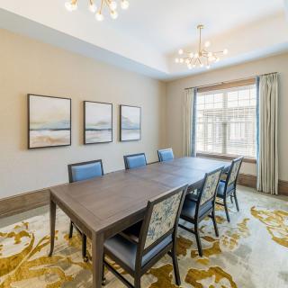 A spacious dining room featuring a large table with chairs, framed artwork on the wall, and natural light streaming through a window.