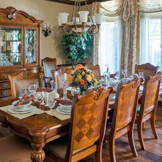 A beautifully set dining table with elegant wooden chairs, a chandelier overhead, and decorative curtains enhancing the ambiance.