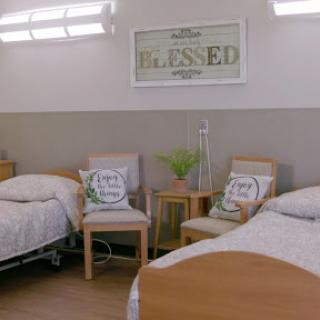 A welcoming and clean hospital patient room with two beds, decorated with cushions and a positive message.