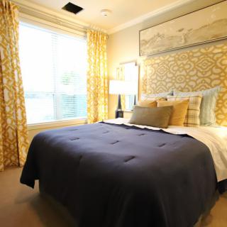A well-decorated bedroom featuring a large bed with pillows and a dark comforter, surrounded by patterned curtains and soft lighting.