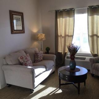 A cozy living room with a sofa and armchair arranged around a coffee table, illuminated by a standing lamp near the window.