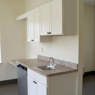 Minimalist apartment kitchen with white cabinets and a single sink.