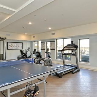 A well-equipped gym featuring treadmills, ellipticals, stationary bikes, and a ping pong table.