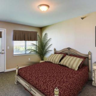 A well-decorated bedroom featuring a large bed with patterned bedding, a window with blinds, and a small indoor plant.