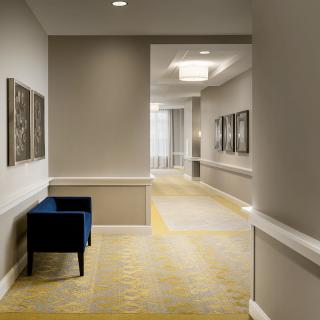 A modern hotel hallway with artwork on the walls and a blue chair against a beige backdrop.