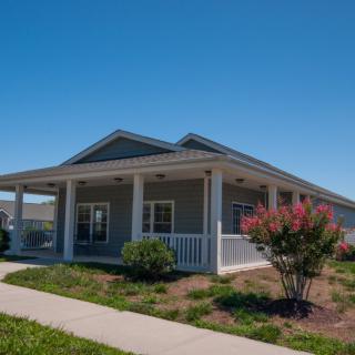 A single-story house with a spacious porch and landscaped garden under a clear blue sky.