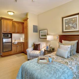 A cozy bedroom with a small kitchenette, featuring a comfortable bed and seating area.