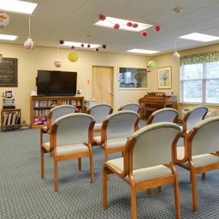 An empty waiting room with chairs arranged in rows facing a television and bookshelf.