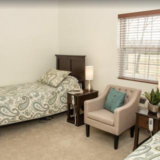 A cozy bedroom with a single bed, a nightstand, and a comfortable armchair by the window.
