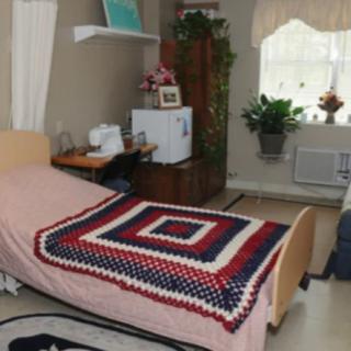 A cozy room with a hospital bed adorned by a colorful crochet blanket, featuring a plant and window that allow natural light to fill the space.